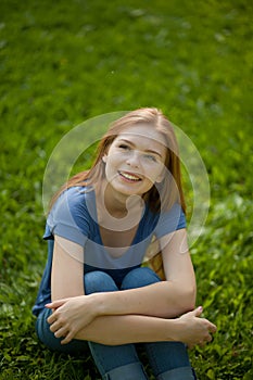 Beautiful red-haired girl sitting on grass