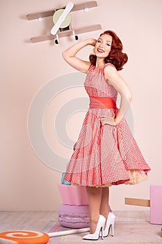 Beautiful red-haired pinup smiling happily girl posing in a retro red dress and white high heels