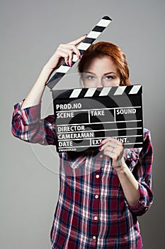 Beautiful red-haired woman holding a movie clapper, isolated over gray background.
