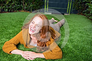 Beautiful red-haired woman lies on the lawn and takes pleasure