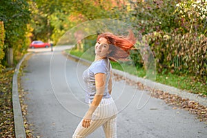 A beautiful red-haired woman walks in the park on a warm autumn day. The girl turns around.