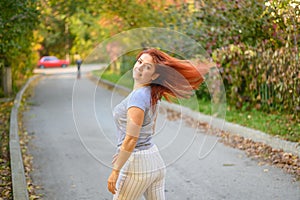 A beautiful red-haired woman walks in the park on a warm autumn day. The girl turns around.
