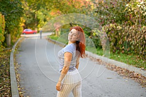 A beautiful red-haired woman walks in the park on a warm autumn day. The girl turns around.