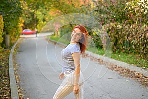 A beautiful red-haired woman walks in the park on a warm autumn day. The girl turns around.