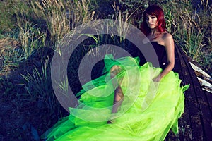 Beautiful red haired womanin black corset and long tail green veiling skirt lying on the shabby upside down wooden boat