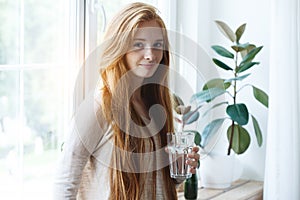 Beautiful red haired young woman holding glass of pure water to drink