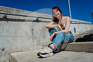 Beautiful red-haired young woman with a smile sitting on a staircase outdoors