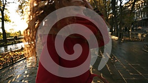 Beautiful red head young woman joyfully running in a colorful autumn park by alley, enjoying autumn foliage, turns