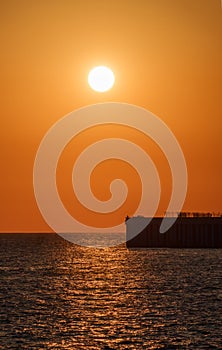 Beautiful red and orange sunset over the sea. The sun goes down over the sea. Silhouette of a pier with fishermen at sunset