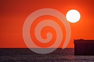 Beautiful red and orange sunset over the sea. The sun goes down over the sea. Silhouette of a pier with fishermen at sunset