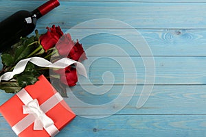 Beautiful red roses, gift box and bottle of wine on light blue wooden background, flat lay with space for text. Valentine`s Day