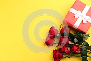 Beautiful red roses and gift box on yellow background, flat lay with space for text. Valentine`s Day celebration