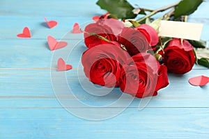 Beautiful red roses and paper hearts on light blue wooden table. Valentine`s Day celebration