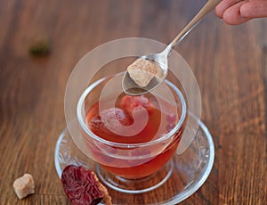 Beautiful red tea. Berry tea with red leaves on a blurred background. Woman with a spoon of sugar and a cup. Copy space.