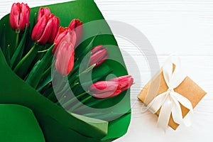 Beautiful red tulips bouquet in green paper and gift box on white wooden background flat lay. Happy mothers day. Pink tulips close