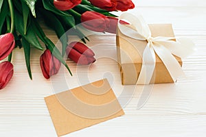 Beautiful red tulips with gift box and craft card with space for text on white wooden background. Happy Mothers day. Pink tulips