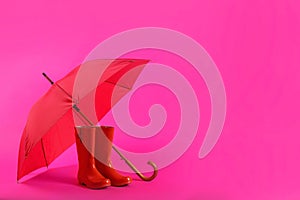 Beautiful red umbrella and rubber boots on pink background