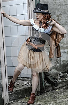 Beautiful redhair steampunk girl with goggles on black hat outside toilet background. Old-fashioned