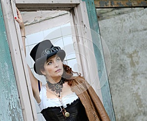 Beautiful redhair steampunk girl with goggles on black hat outside toilet background. Old-fashioned