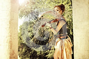 Beautiful redhair woman with body art on her face playing on violin outdoors. photo