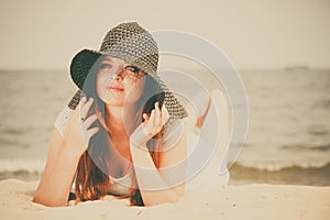 Beautiful redhaired happy girl in black hat on beach.
