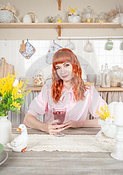 Beautiful redhaired woman with glass of wine sitting in the kitchen at home