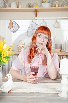 Beautiful redhaired woman with glass of wine sitting in the kitchen at home