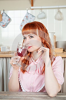 Beautiful redhaired woman with glass of wine sitting in the kitchen at home