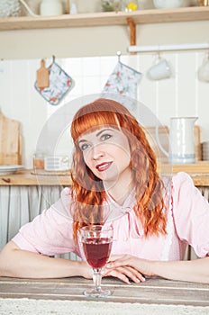 Beautiful redhaired woman with glass of wine sitting in the kitchen at home