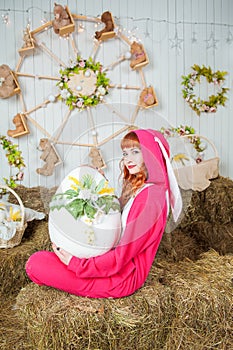 Beautiful redhaired woman wearing bunny costume with big egg sitting on the haystack Easter holiday concept