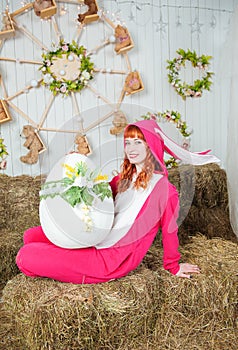 Beautiful redhaired woman wearing bunny costume with big egg sitting on the haystack Easter holiday concept