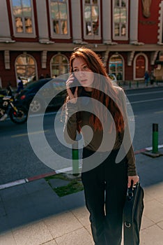 Beautiful redhead business girl talking on phone while carrying a lap top case