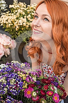 Beautiful redhead Caucasian girl smelling colorful flowers in the garden
