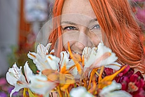 Beautiful redhead Caucasian girl smelling colorful flowers in the garden