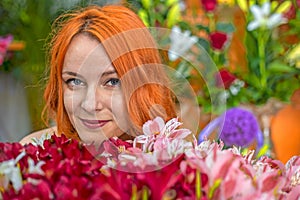 Beautiful redhead Caucasian girl smelling colorful flowers in the garden