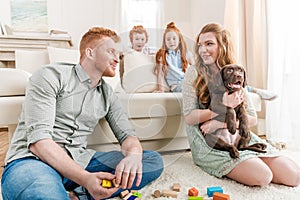 Beautiful redhead family with puppy playing with constructor on floor at home