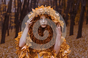 Beautiful redhead girl as an autumn in leaf cloak in forest background beauty portrait photoshoot