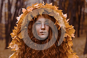 Beautiful redhead girl as an autumn in leaf cloak in forest background beauty portrait photoshoot