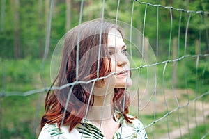 Beautiful redhead girl behind fence outdoors.