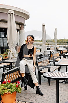 Beautiful redhead girl with a cup of coffee sits on the street