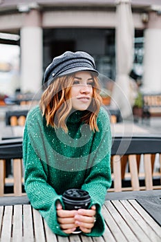 Beautiful redhead girl with a cup of coffee sits on the street