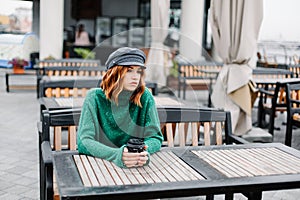 Beautiful redhead girl with a cup of coffee sits on the street