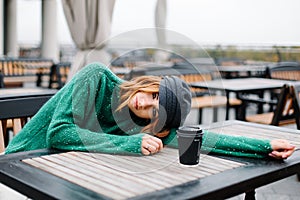 Beautiful redhead girl with a cup of coffee sits on the street