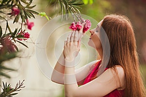 Beautiful redhead girl inhales the aroma of the flower. Red flower growing on a tree.