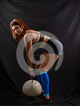 Beautiful redhead girl lifts a huge kettlebell in the studio on a black background