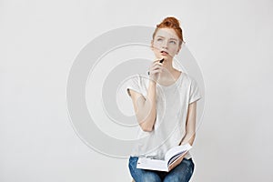 Beautiful redhead girl making notes thinking sitting over white background.