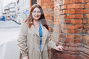 Beautiful redhead girl posing outdoors. Outdoor fashion portrait of elegant, luxury woman wearing beige coat. Urban