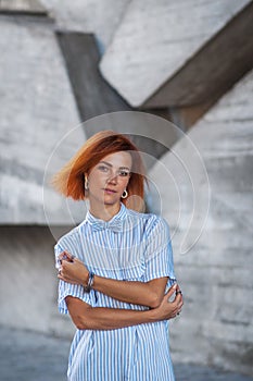 Beautiful redhead girl wearing in a striped shirt posing against background of concrete wall