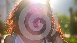 A beautiful redhead with long fiery curly hair in a white dress with glasses walks around the city and prints sms on the