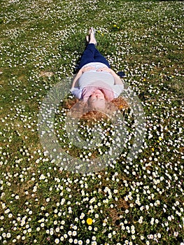 Beautiful redhead mature woman in her fifties lies contentedly in the grass and enjoys the sun in a field of daisies